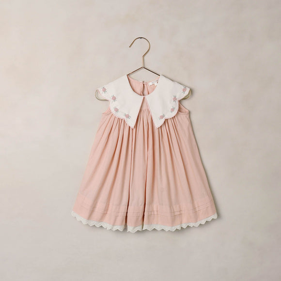 Pink dress with white collar on a hanger against a beige background