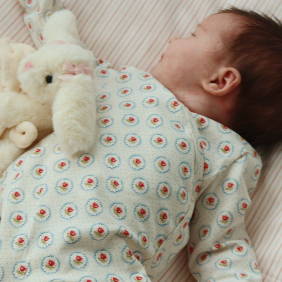 Baby in a floral onesie holding a plush toy on a soft surface