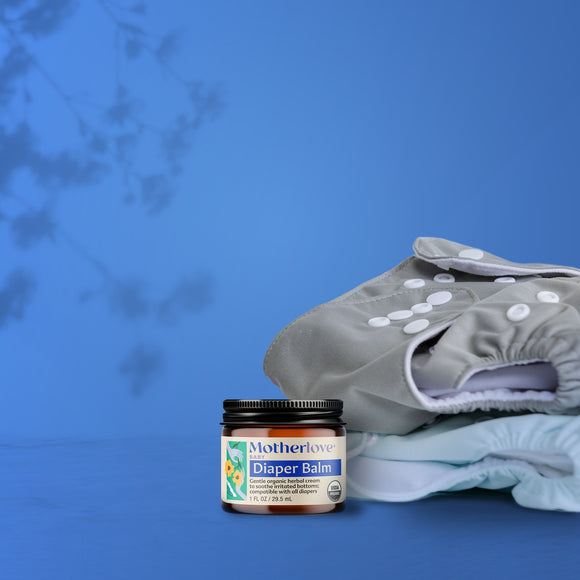 Jar of Motherlove Diaper Balm with a stack of diapers on a blue background