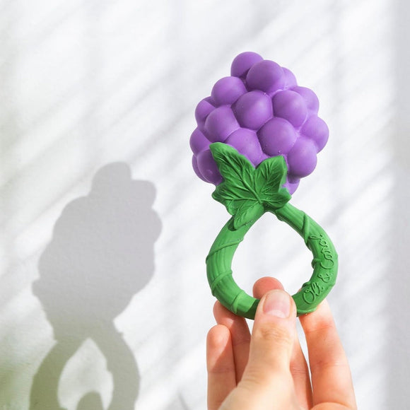 Purple and green teething toy shaped like grapes held by a hand against a white background
