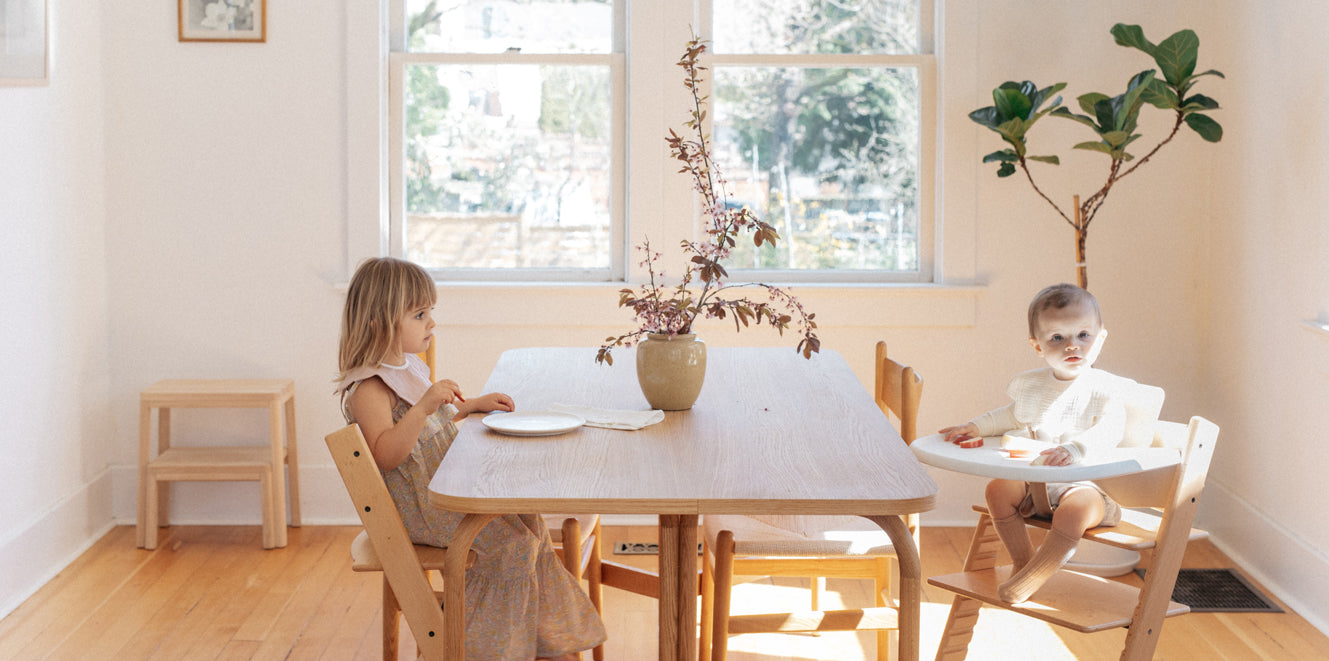 Toddler and baby in high chair eating at table